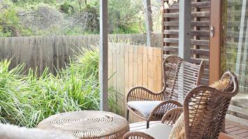 A wicker outdoor seating area with a round table, a wooden fence, and a view of greenery.