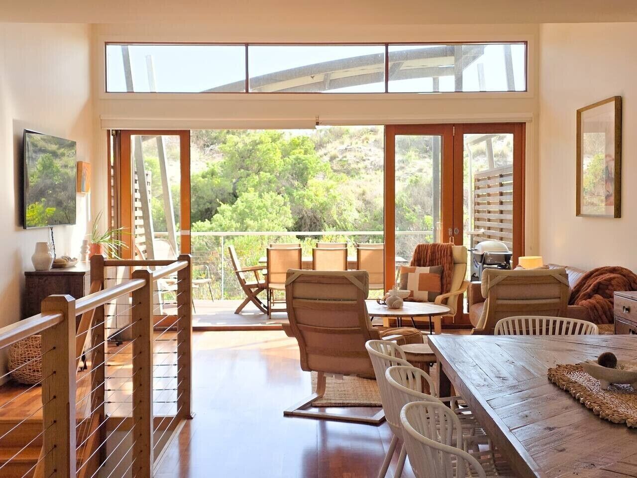 A spacious room with a large sliding glass door leading to a balcony, wooden furniture, and a view of greenery.