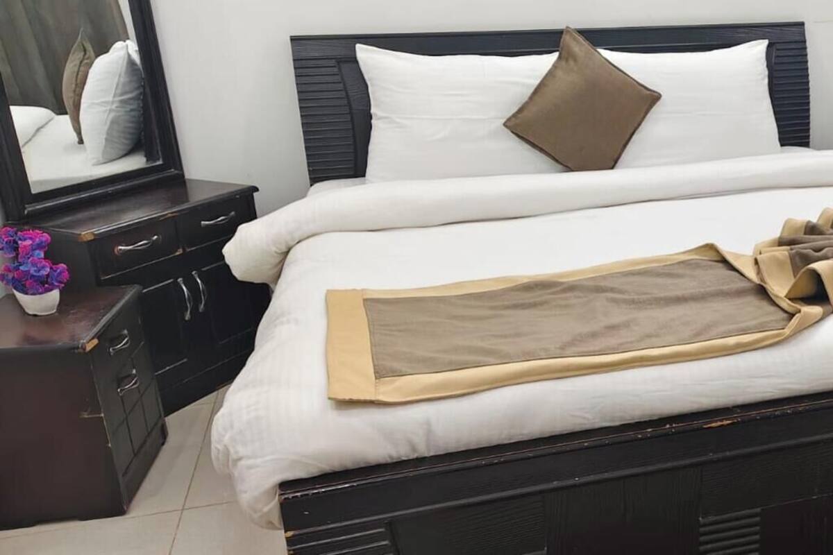 Una cama bien hecha con una colcha blanca, un edredón marrón y un arreglo decorativo de telas.