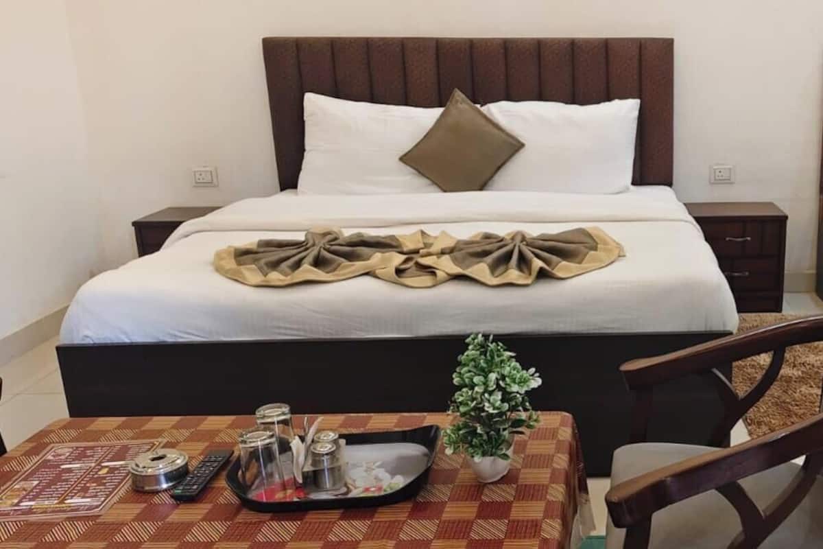 Una habitación de hotel con una cama grande, otra más pequeña, una mesa de comedor con una bandeja y una planta pequeña.