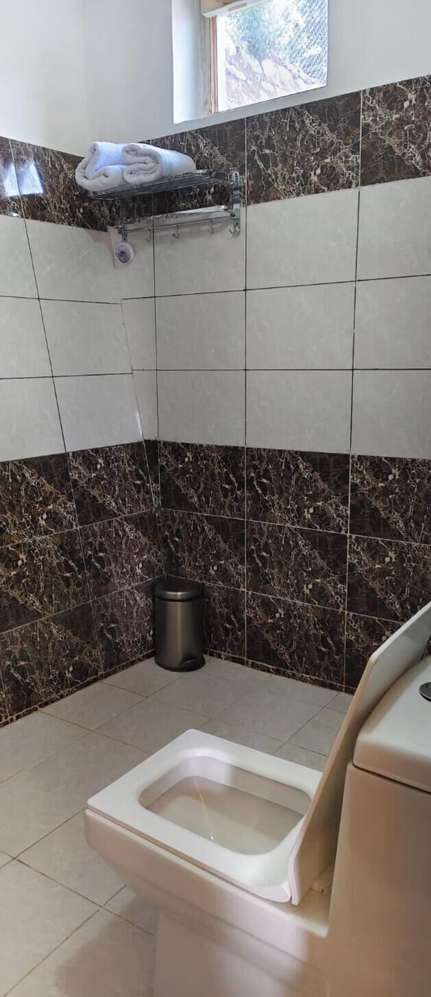 A bathroom with a toilet, a trash bin, and a shelf with towels.