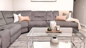 A modern living room with a grey sectional sofa, a glass coffee table, and a framed picture on the wall. - Central Arlington Gem Near AT&T Stadium & Texas Live 2BR (Arlington)