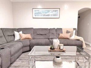 Una sala moderna con un sofá modular gris, una mesa de centro de cristal y un cuadro enmarcado en la pared.