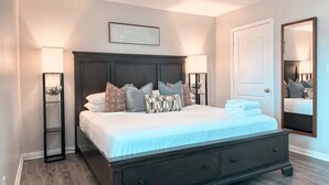 A bedroom with a dark wood bed, two bedside tables, a ceiling fan, a large mirror, and a door. - Central Arlington Gem Near AT&T Stadium & Texas Live 2BR (Arlington)