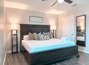 A bedroom with a dark wooden bed, two bedside lamps, a ceiling fan, a large mirror, and a framed quote on the wall. - Central Arlington Gem Near AT&T Stadium & Texas Live 2BR (Arlington)