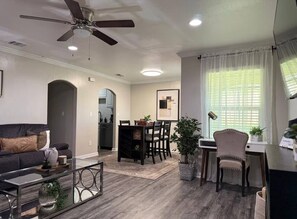 A modern living room with a sofa, coffee table, dining area, and a ceiling fan. - Central Arlington Gem Near AT&T Stadium & Texas Live 2BR (Arlington)