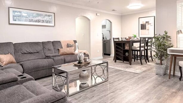 A modern living room with a grey sofa, a glass coffee table, and a dining area with a wooden table and chairs. - Central Arlington Gem Near AT&T Stadium & Texas Live 2BR (Arlington)