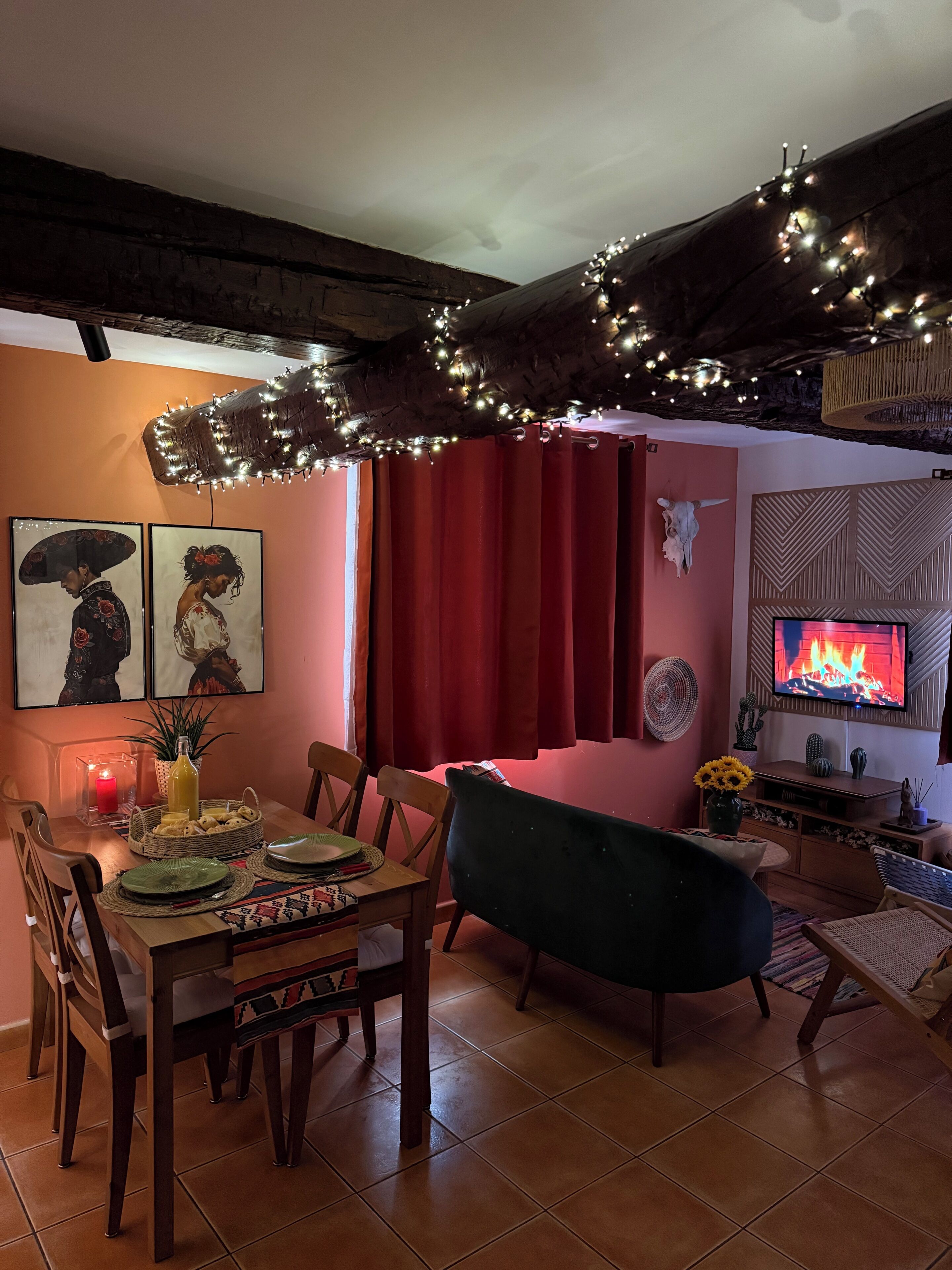 Ein Essbereich mit einem Holztisch, Stühlen, einem Fernseher, der ein Feuer zeigt, und einem roten Vorhang.