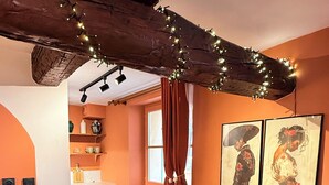 Un coin repas avec une table en bois, des chaises et un sol carrelé. On y trouve des étagères fixées au mur, sur lesquelles sont disposés de la vaisselle et une plante en pot.