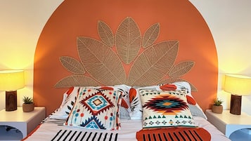 Un lit avec une couvre-lit à motifs géométriques, deux coussins ornés de motifs tribaux, un élément décoratif en forme de feuille fixé au mur et des lampes de chevet.