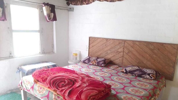 Um quarto com cama, mesa de cabeceira, janela e tomadas na parede.