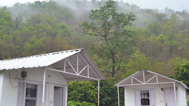 Two white buildings with metal roofs, surrounded by dense green forest and mist. - Raiseraa Cottages (Lansdowne)