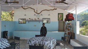 A covered outdoor seating area with tables and chairs, a man standing, and a ladder against the wall. - Raiseraa Cottages (Lansdowne)