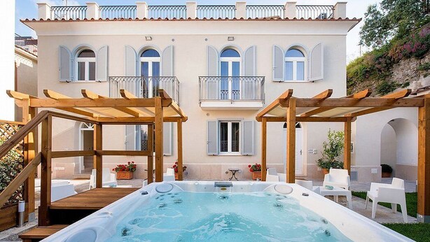 Un área de spa con jacuzzi, pérgolas de madera y mobiliario exterior.