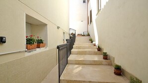 Una escalera estrecha flanqueada por macetas, que conduce a un piso superior.