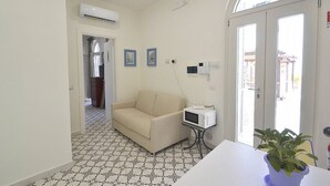 Una habitación con sofá, microondas, planta en maceta y suelo de baldosas.