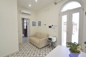 Ein Zimmer mit einer Couch, einer Mikrowelle, einem Blumentopf und einem gefliesten Boden.