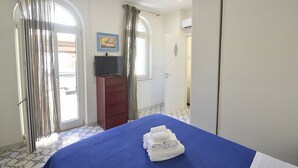 Habitación de hotel con cama, televisión, armario y puerta que da a otra habitación.