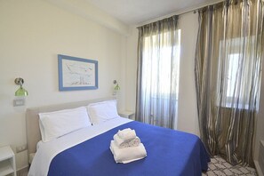 Ein Hotelzimmer mit Bett, einem gerahmten Bild an der Wand und einem Fenster mit Vorhängen.
