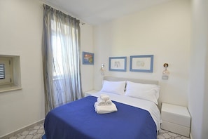Ein Hotelzimmer mit einem Bett, einem Nachttisch, einem Fenster mit Vorhängen und Wandbildern.