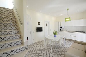 Eine moderne Küche mit weißen Schränken, einem Esstisch mit Stühlen, einer Treppe mit gemusterten Fliesen und einer grünen Pendelleuchte.