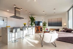 Eine moderne Küche mit Barhocker, einem Essbereich mit einer Couch und einem großen Fenster.