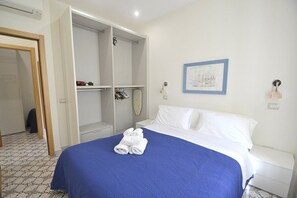 Ein Hotelzimmer mit Bett, Kleiderschrank, einem gerahmten Bild an der Wand und Fliesenboden.