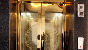 Un ascensor con puertas de vidrio reflectante, panel de control y suelo con diseño.