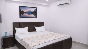 Un dormitorio con cama, mesita de noche, aire acondicionado de pared y un cuadro con un paisaje de montaña.