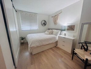 Ein Schlafzimmer mit Bett, Nachttisch, Lampe, Sessel und einer kleinen Pflanze.
