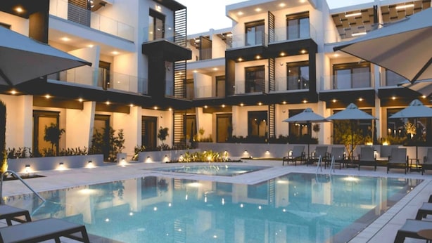 A modern building with a pool, outdoor seating, and multiple balconies. - Villa Elegance in Nikiti (Sithonia)