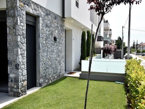 A modern building with a stone facade, a well-maintained lawn, and a clear view of the street. - Villa Elegance in Nikiti (Sithonia)