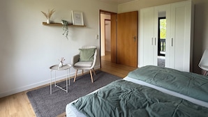 Una camera da letto con un letto, una sedia, un tavolino, uno scaffale con piante, una porta e un armadio.