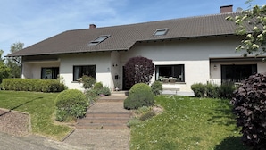 Una casa a due piani con tetto in tegole, un portico e un prato curato.