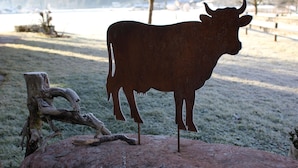 Une sculpture de vache en métal, posée sur un rocher, avec un paysage naturel en arrière-plan.
