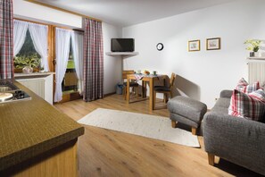 A cozy living room with a sofa, a small table, and a TV mounted on the wall. - Vacation apartment Watzmann, 25 sqm, 1-2 persons, 1 separate bedroom, balcony (Schönau am Königssee)