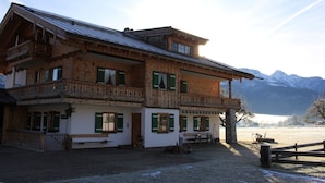 Un chalet en bois doté de plusieurs balcons, d’une terrasse en bois et offrant une vue sur des montagnes enneigées en arrière-plan.