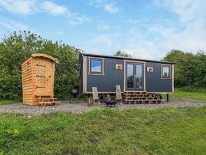 En hyggelig hytte med et træskur, grill og en græsplæne med belægning.