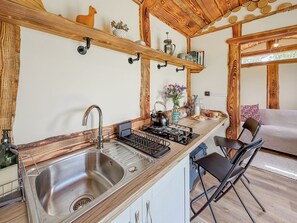 Et køkken med en stålvask, træhylder, en elkedel og et spiseområde med en stol og et bord.