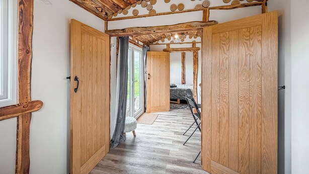 A wooden interior with a hallway leading to a bed area, a small round table, and a bench. - 1 bedroom accommodation in Corwen (Corwen)