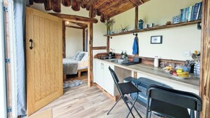 Een compacte keuken met houten kasten, een eethoek met stoelen en een zichtbare deur naar een andere kamer.