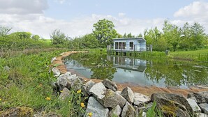 Een huis op palen boven een vijver, omringd door groen.