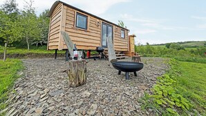Een houten hut met een terras, een barbecue en een vuurkuil.