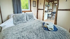 Een slaapkamer met een bed, een raam met gordijnen, een houten plafond en uitzicht op een keuken.