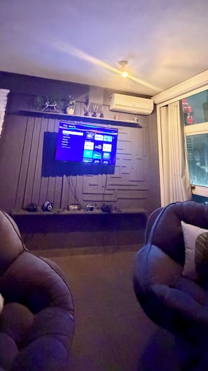 Ein Wohnzimmer mit einem Wand-Fernseher, einem Kamin und zwei Ledersesseln.