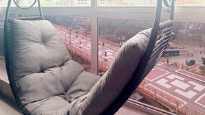 Uma cadeira suspensa em um quarto com uma janela grande que dá para a paisagem urbana.