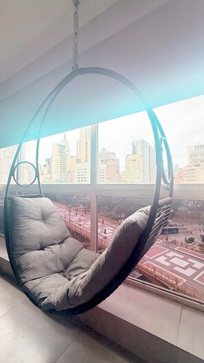 Ein Hängestuhl in einem Zimmer mit einem großen Fenster und Blick auf die Stadt.