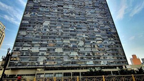 Um edifício alto e moderno com fachada em grade, rodeado por um piso padronizado e um guarda-corpo decorativo.