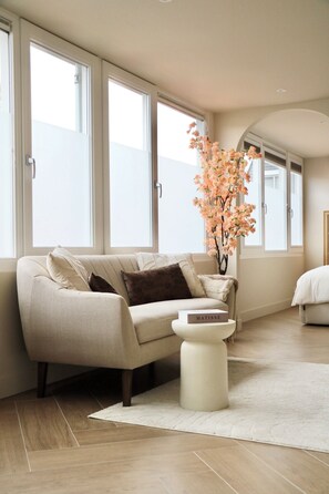 A modern living room with a beige sofa, a white side table, and a vase with flowers. - Breeze Inn - Japandi apartment - Strand, Leiden, Bioscience Park (Oegstgeest)