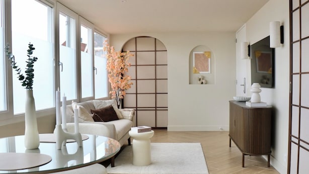 A modern living room with a sofa, a glass coffee table, a white vase, and a decorative plant.